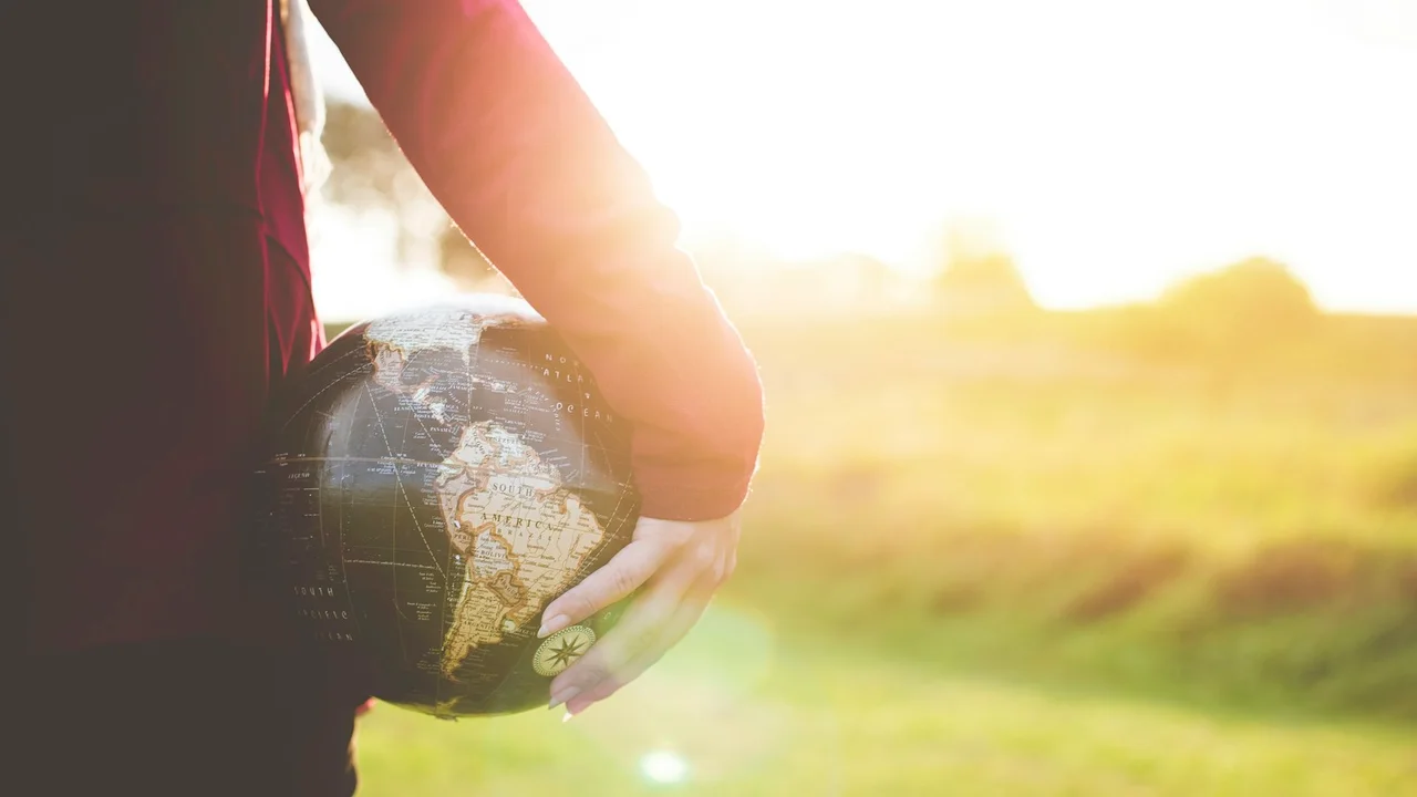 person holding black and brown globe ball while standing on grass land golden hour photography