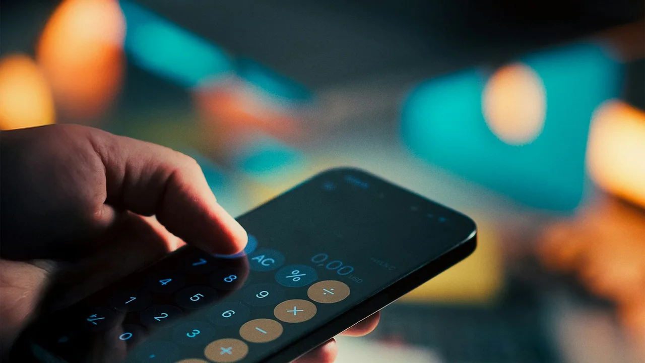 Hand using calculator on smartphone over money
