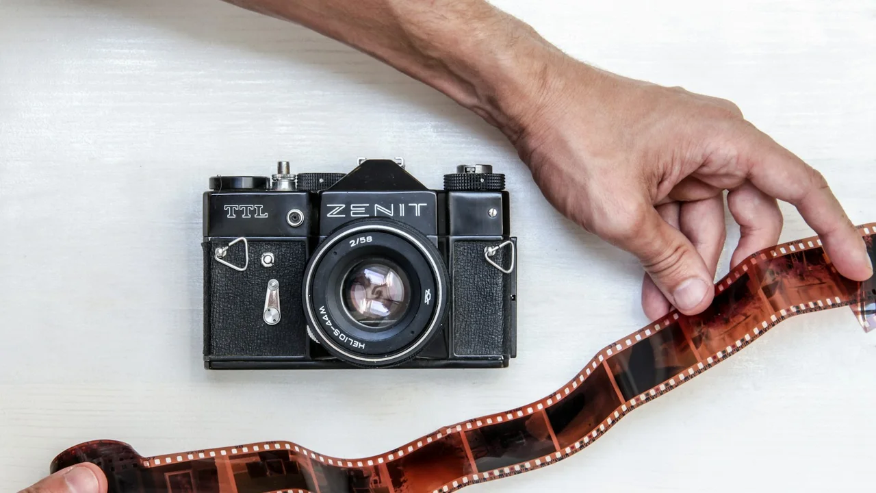 flat lay photography of person showing photo film beside Zenit DSLR camera